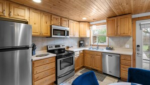 A modern kitchen with wooden cabinets, stainless steel appliances, and a view to the outside. - "cozy Cottages" Blue Cottage-hot Tub/town! (Saugatuck)