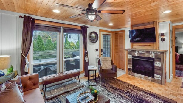 Un salon chaleureux avec un ventilateur de plafond, de grandes fenêtres, une cheminée et un coin salon confortable.