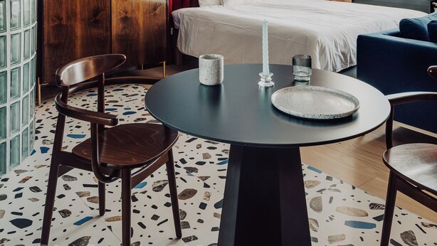 A hotel room with a bed, a round table with a candle, a chair, a wardrobe, and a large window. - Apartament przy MCK (Katowice)