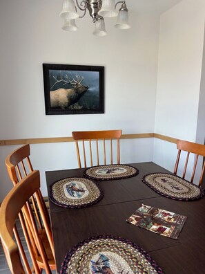 A dining area with a dark wooden table, four wooden chairs, and a framed wildlife painting on the wall.