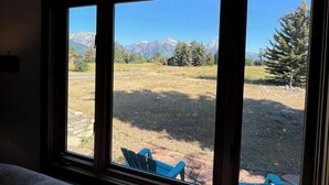 Una habitación con un ventanal grande que da a un campo cubierto de hierba y montañas.