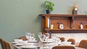 A dining table set with white plates and glasses, a potted plant, and a decorative shelf with a vase and a small figurine.