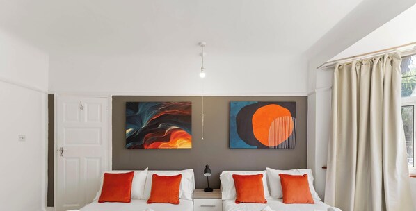 A bedroom with two beds, a door, and two abstract paintings on the wall.