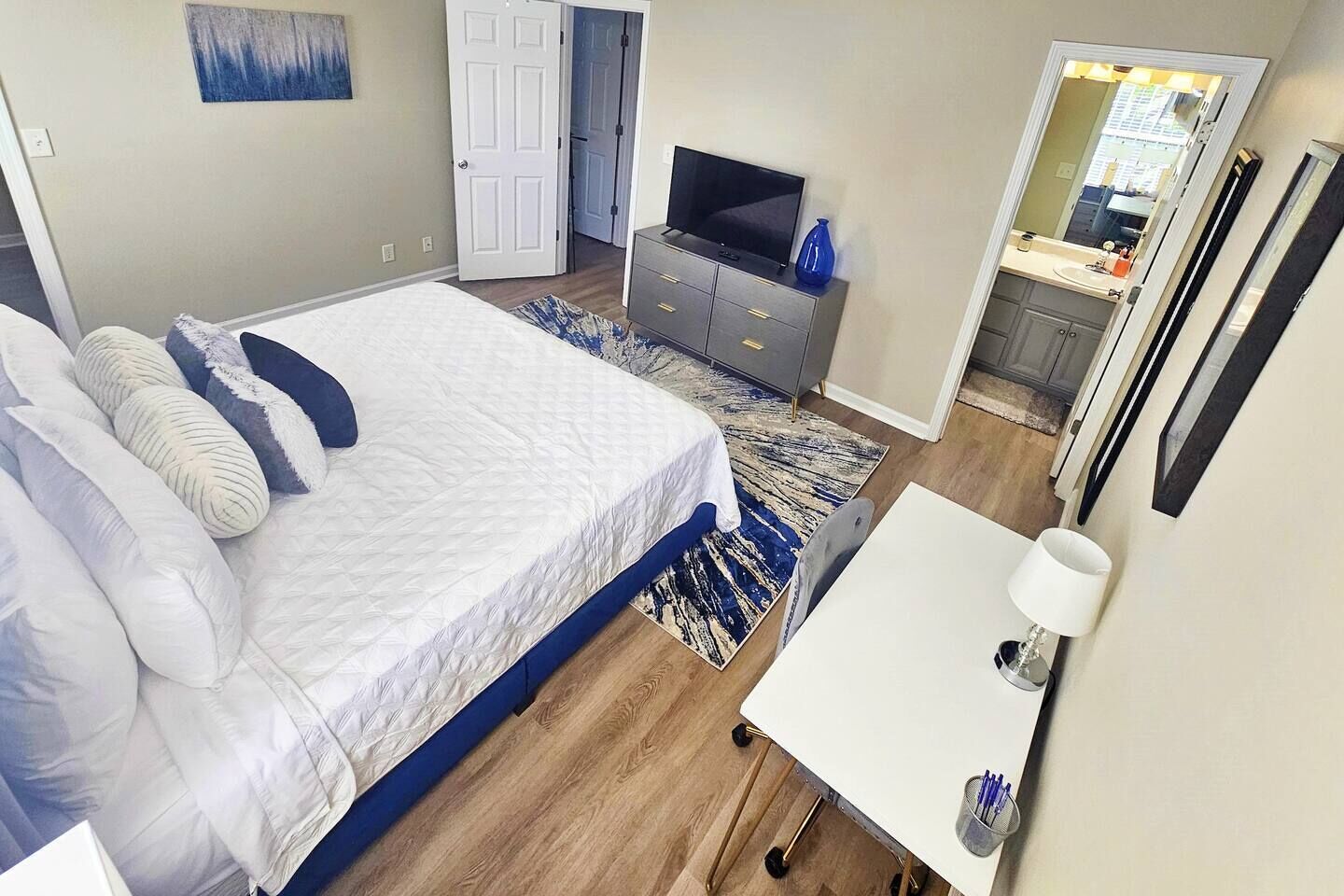 Une chambre à coucher avec un lit, une commode, un téléviseur et une salle de bain visible à travers une porte ouverte.