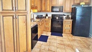 Una cucina con mobili in legno, un frigorifero nero, un forno a microonde, un fornello e una lavastoviglie.