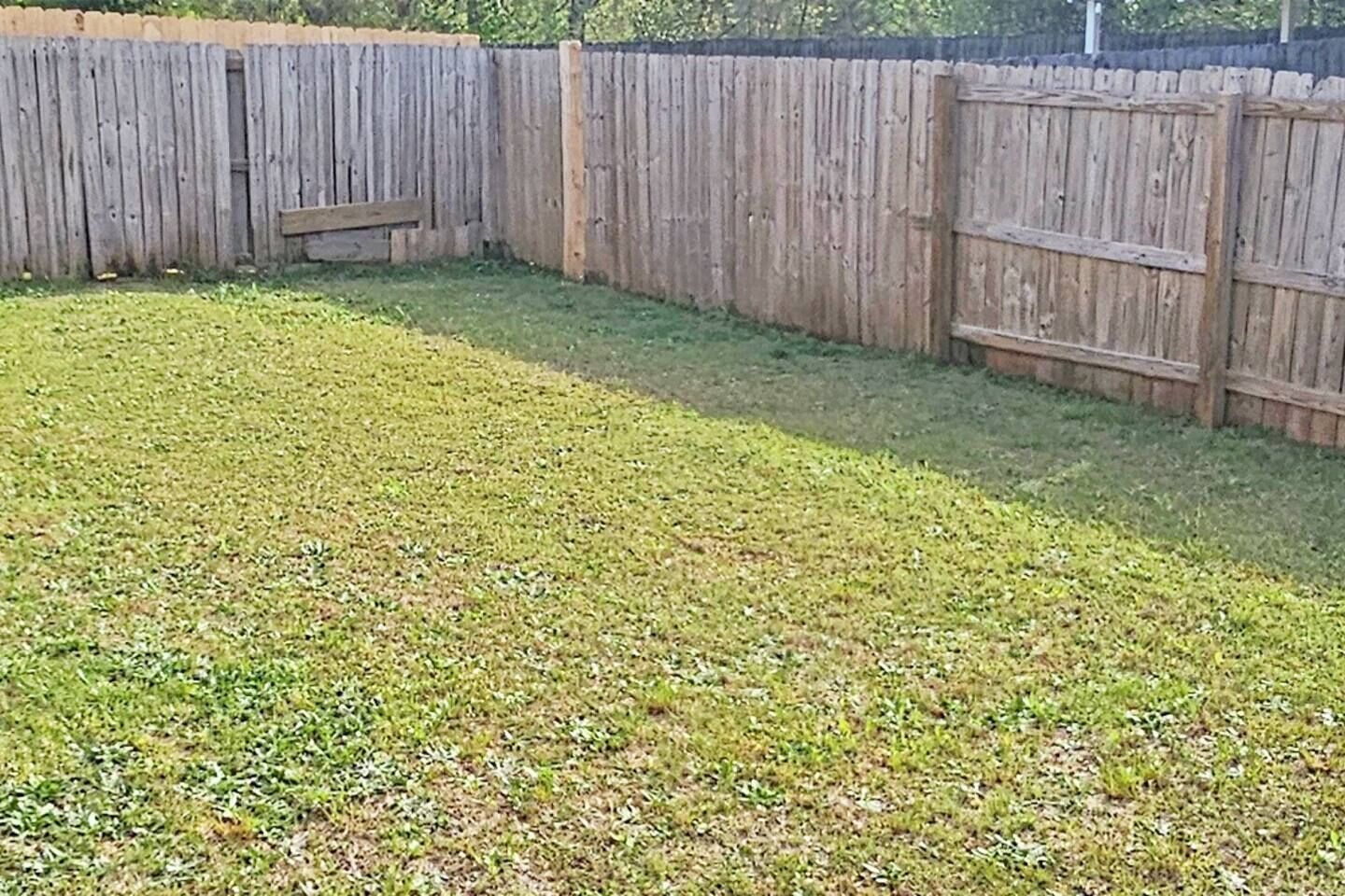 A backyard with a wooden fence, a grassy lawn, and a small patch of dirt.