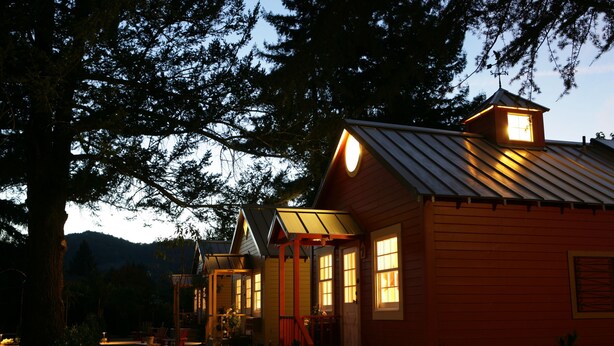 A rustic cabin with a metal roof, wooden walls, and a porch area with chairs.