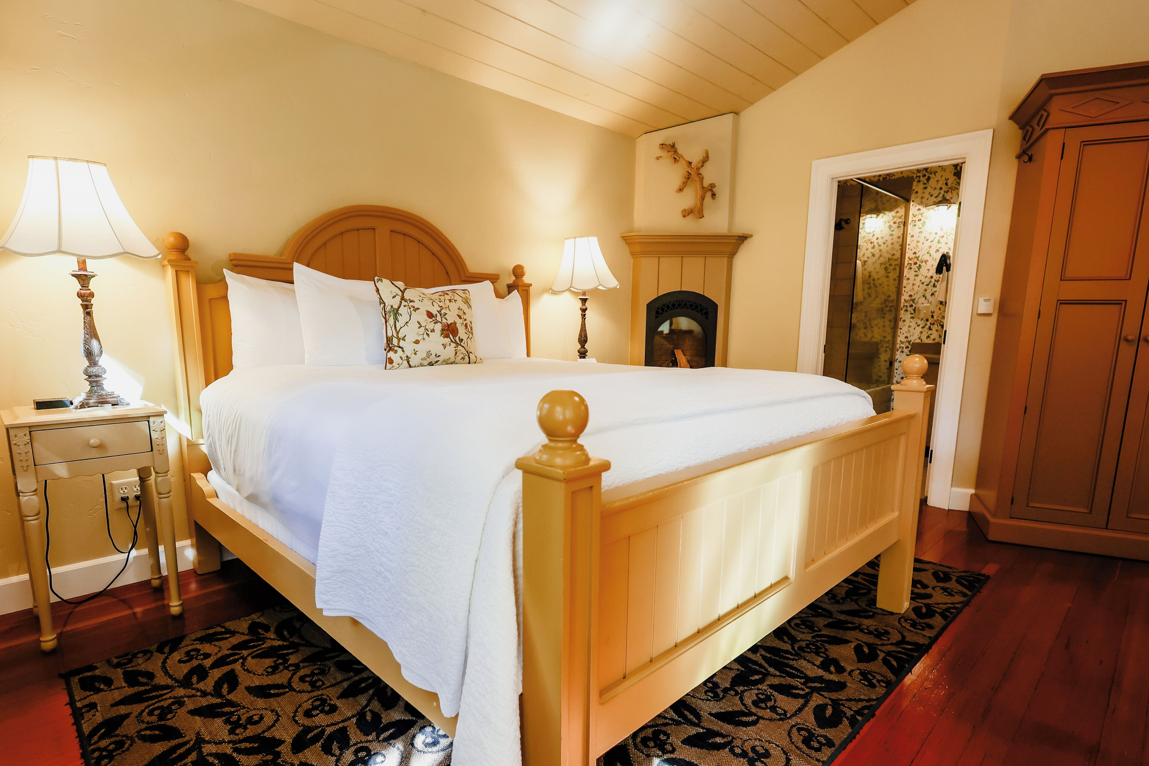 A bedroom with a wooden bed, two bedside tables with lamps, a fireplace, and a wardrobe.