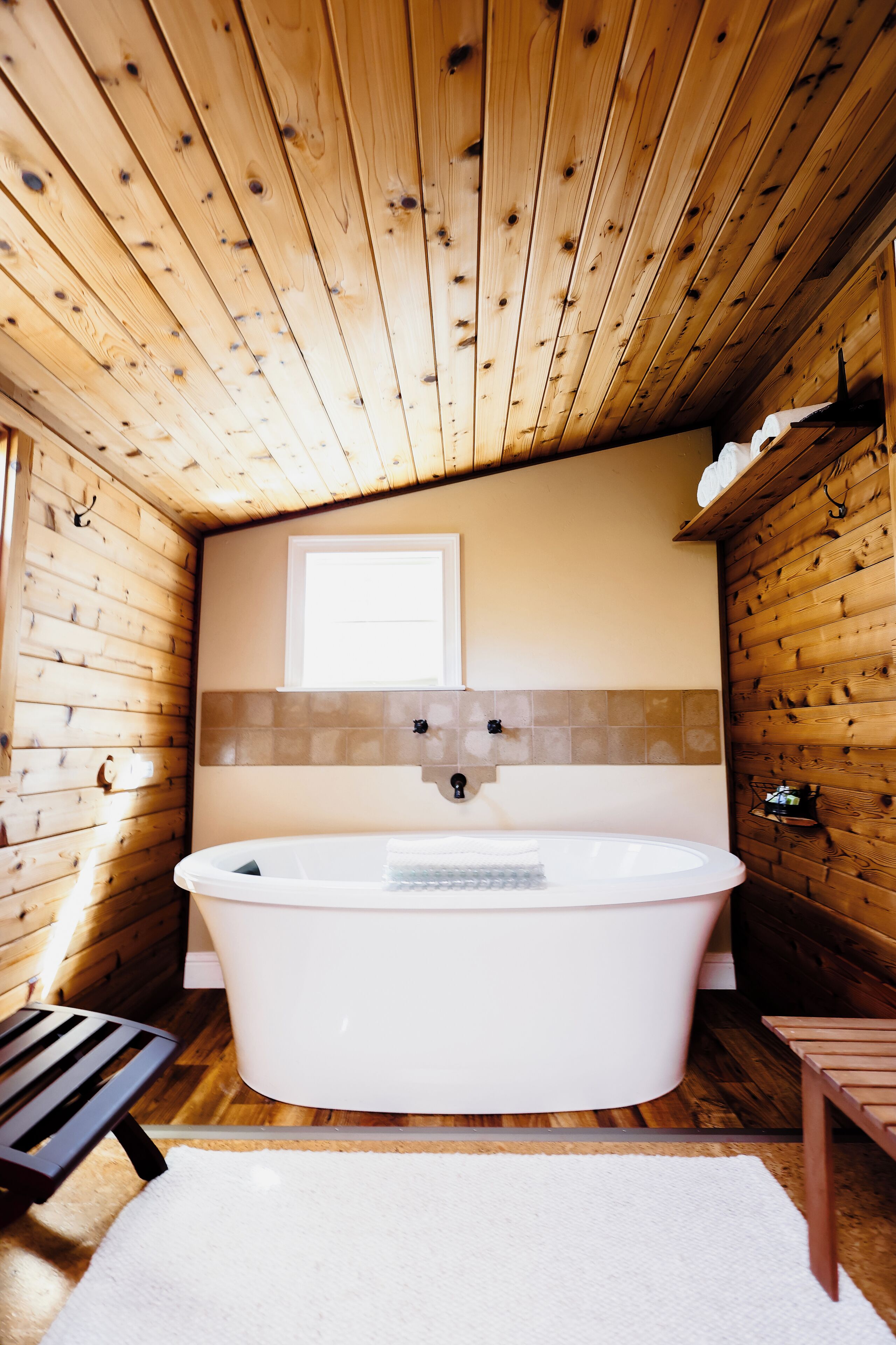 A wooden cabin interior with a large bathtub, a window, and a wooden bench.