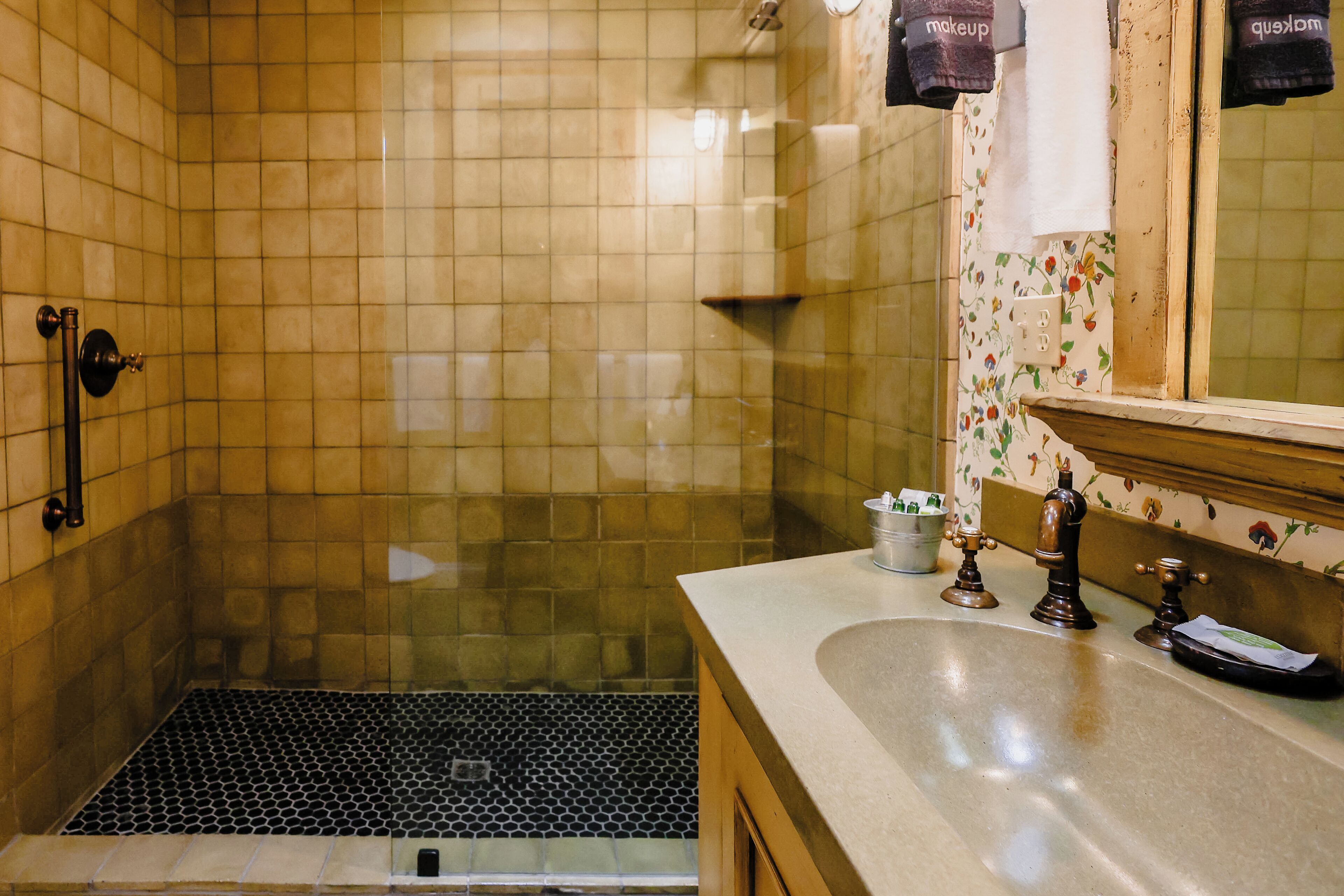 A bathroom with a shower, a sink with a mirror, and a tiled floor.