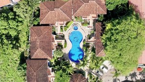 An aerial view of a resort with multiple buildings, a central swimming pool, and surrounding palm trees. - 2-bedroom condo in beautiful Playa Del Coco.  5 minute walk to beach (Guanacaste Province)