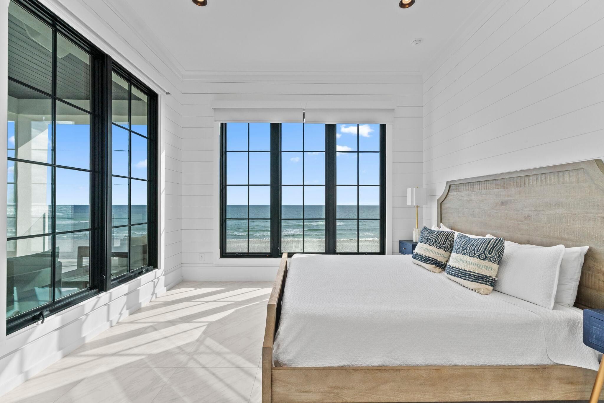 Une chambre avec une grande fenêtre donnant sur l’océan, un lit en bois et une vue sur la plage.