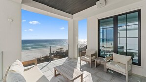 Ein Balkon mit Blick auf den Strand, eine hölzerne Bank und ein gepolsterter Stuhl.