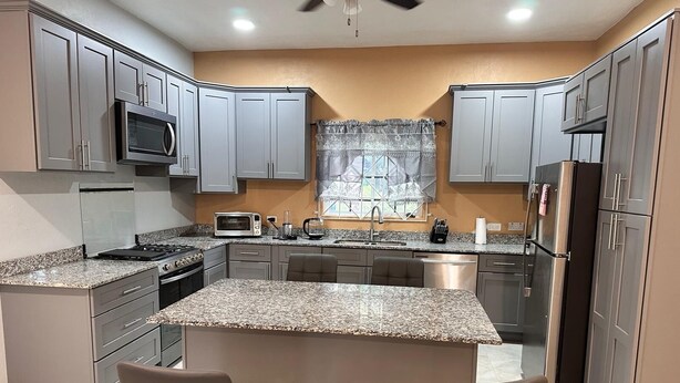 Cocina moderna con encimeras de granito, electrodomésticos de acero inoxidable y armarios grises.