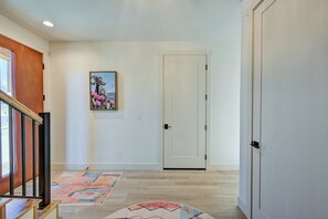 Un pasillo con una escalera de madera, una puerta blanca y un tapete colorido.