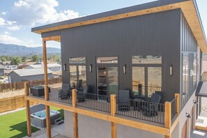 A modern two-story building with a balcony, outdoor seating, and a hot tub.