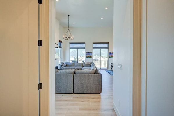 A modern living room with a sectional sofa, large windows, and a chandelier.