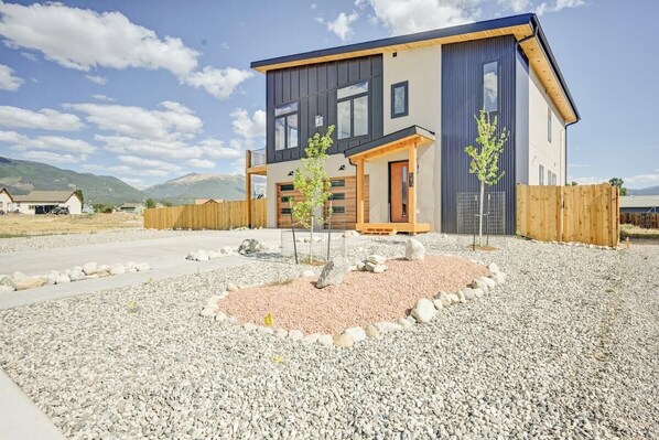 A modern two-story house with a flat roof, a wooden fence, and a gravel driveway.