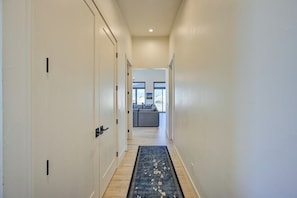 A hallway with a carpet leading to a living area with a sofa and a window.