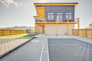 A modern two-story building with a balcony, a basketball court, and a view of the mountains.