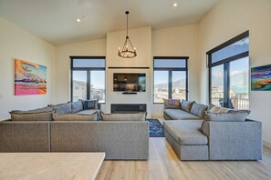 Un salón amplio con un sofá seccional grande, una chimenea y ventanas grandes que ofrecen vistas a la montaña.
