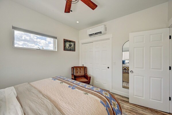 Un dormitorio con cama, una silla, un ventanal, un equipo de aire acondicionado y una puerta.