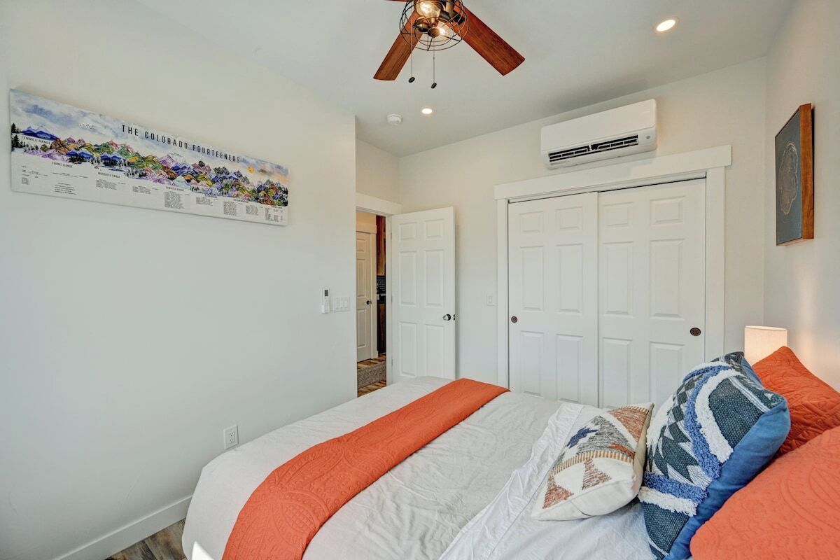 A bedroom with a bed, a ceiling fan, a wall-mounted air conditioner, and a door.