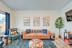 Una sala de estar con un sofá, una mesa de centro redonda, un sillón azul y una planta en maceta.
