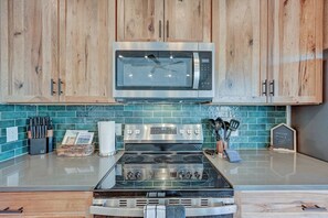 Una cocina con armarios de madera, microondas, estufa y salpicadero de azulejos.