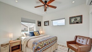 A bedroom with a bed, a chair, a ceiling fan, and framed pictures on the wall.