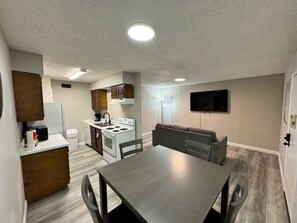 A compact living space with a kitchenette, dining area, and a flat-screen TV mounted on the wall. - 1BR Retreat • Cozy & Bright (Beaumont)