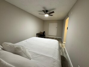 A bedroom with a bed, a desk, a chair, a ceiling fan, and a window with blinds. - 1BR Retreat • Cozy & Bright (Beaumont)