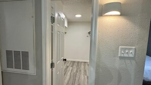 En gang med en hvid dør, en ventilationsrist og en lyskontakt på væggen.