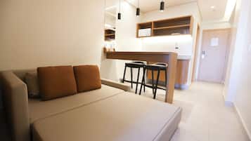 Una habitación de hotel moderna con sofá, una pequeña zona de bar con taburetes, una kitchenette y una puerta que da a otra habitación.