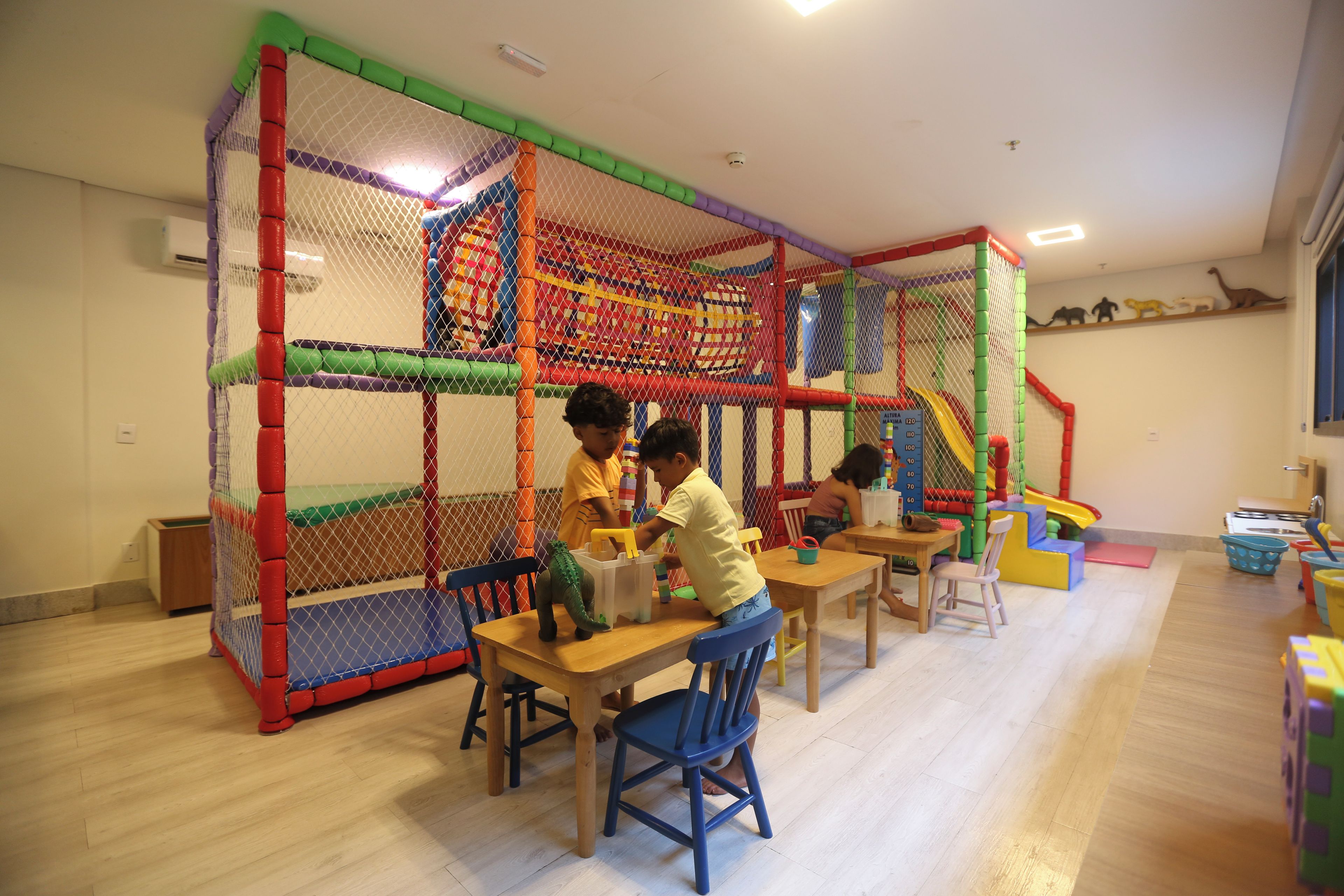 A play area with a netted enclosure, tables, chairs, and a slide.
