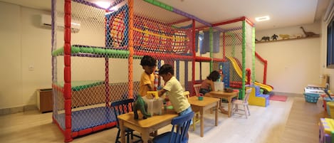 A play area with a netted enclosure, tables, chairs, and a slide.
