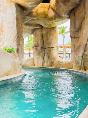 Una piscina con agua turquesa cristalina, rodeada de grandes formaciones rocosas y palmeras.