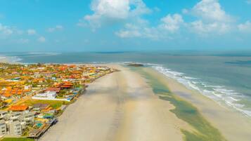 Vista aérea de uma cidade costeira com uma praia, casas com telhados laranja e céu claro.