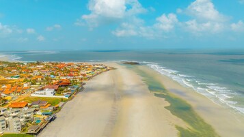 Vista aérea de uma cidade costeira com uma praia, casas com telhados laranja e céu claro.
