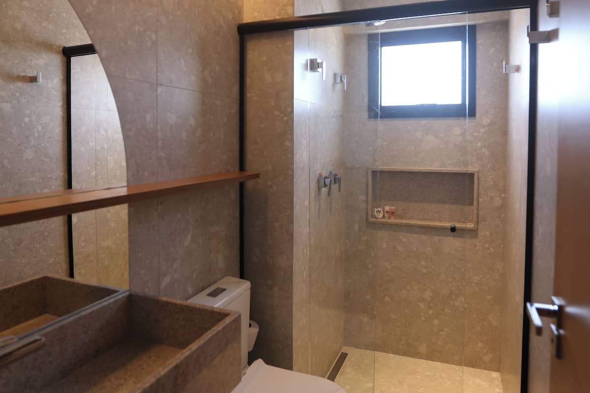 Ein modernes Badezimmer mit einer gläsernen Duschkabine, einer Toilette und einem Waschbecken mit Marmorplatte.