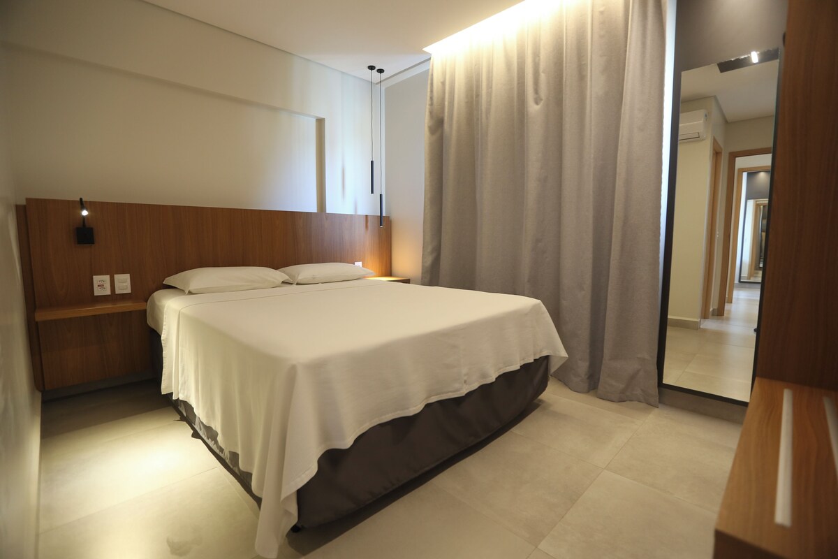 Una habitación de hotel con una cama, una mesita de noche, un espejo y una cortina.