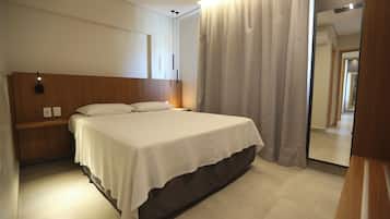 A hotel room with a bed, a nightstand, a mirror, and a curtain.