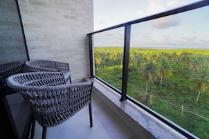 Varanda com cadeiras de vime e vista para uma paisagem verde exuberante com palmeiras.