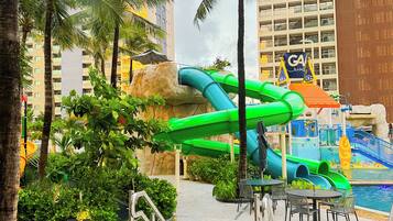 A water park area with slides and palm trees, surrounded by buildings.