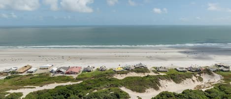A coastal area with a beach, several buildings, and a clear sky.