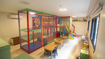 Zona de juegos con cerramiento de red, mesas, sillas y estructuras de juego coloridas.