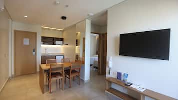 Una habitación de hotel moderna con zona de comedor, un televisor de pantalla plana en la pared y un pequeño estante con folletos informativos.