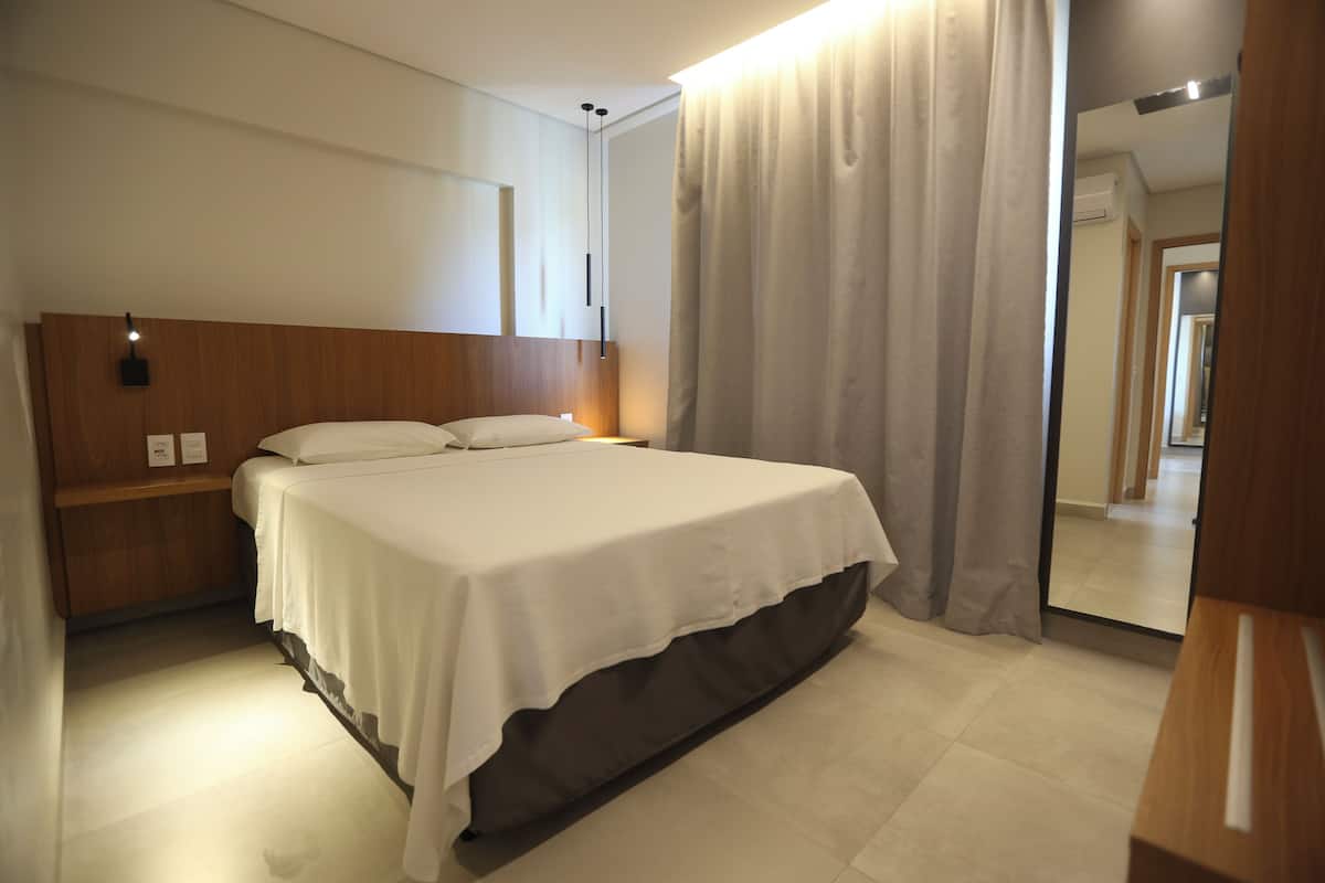 Ein Hotelzimmer mit Bett, Nachttisch, Spiegel und Vorhang.