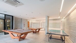 Un'area ricreativa interna moderna con tavoli da biliardo e ping pong, caratterizzata da un design minimalista, tonalità neutre e illuminazione abbondante.