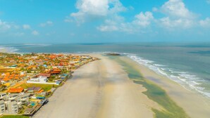 Vista aerea di una località costiera con spiaggia, case dai tetti arancioni e cielo sereno.